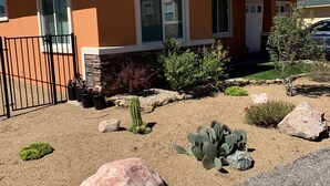 Una casa de un solo piso con fachada color crema, un portón de metal negro y un jardín ajardinado con cactus y rocas.