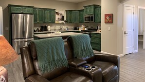 Una cocina moderna con gabinetes verdes, electrodomésticos de acero inoxidable y una zona de estar acogedora con un sofá de cuero y una manta.