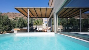 Un espace piscine extérieur moderne, avec une eau d’un bleu limpide, des chaises longues et une structure en forme de pergola.