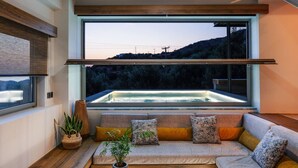 Un intérieur moderne avec une grande fenêtre donnant sur un jacuzzi, un banc en bois et un canapé avec des coussins.
