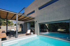 A modern house with a swimming pool, covered patio, and outdoor seating area.