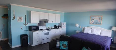A compact room with a bed, a sofa, a kitchenette, and a small trash bin.