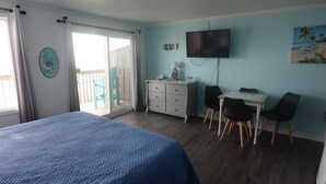 A bedroom with a bed, a desk with two chairs, a TV, and a balcony with chairs. - Sea Vista Motel (Holly Ridge)