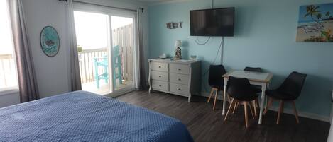 A bedroom with a bed, a desk with two chairs, a TV, and a balcony with chairs.