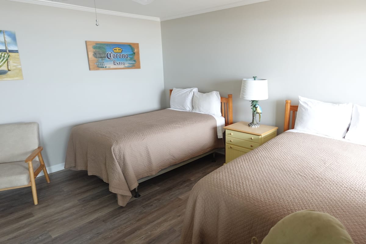 A hotel room with two beds, a nightstand, a lamp, and a chair.