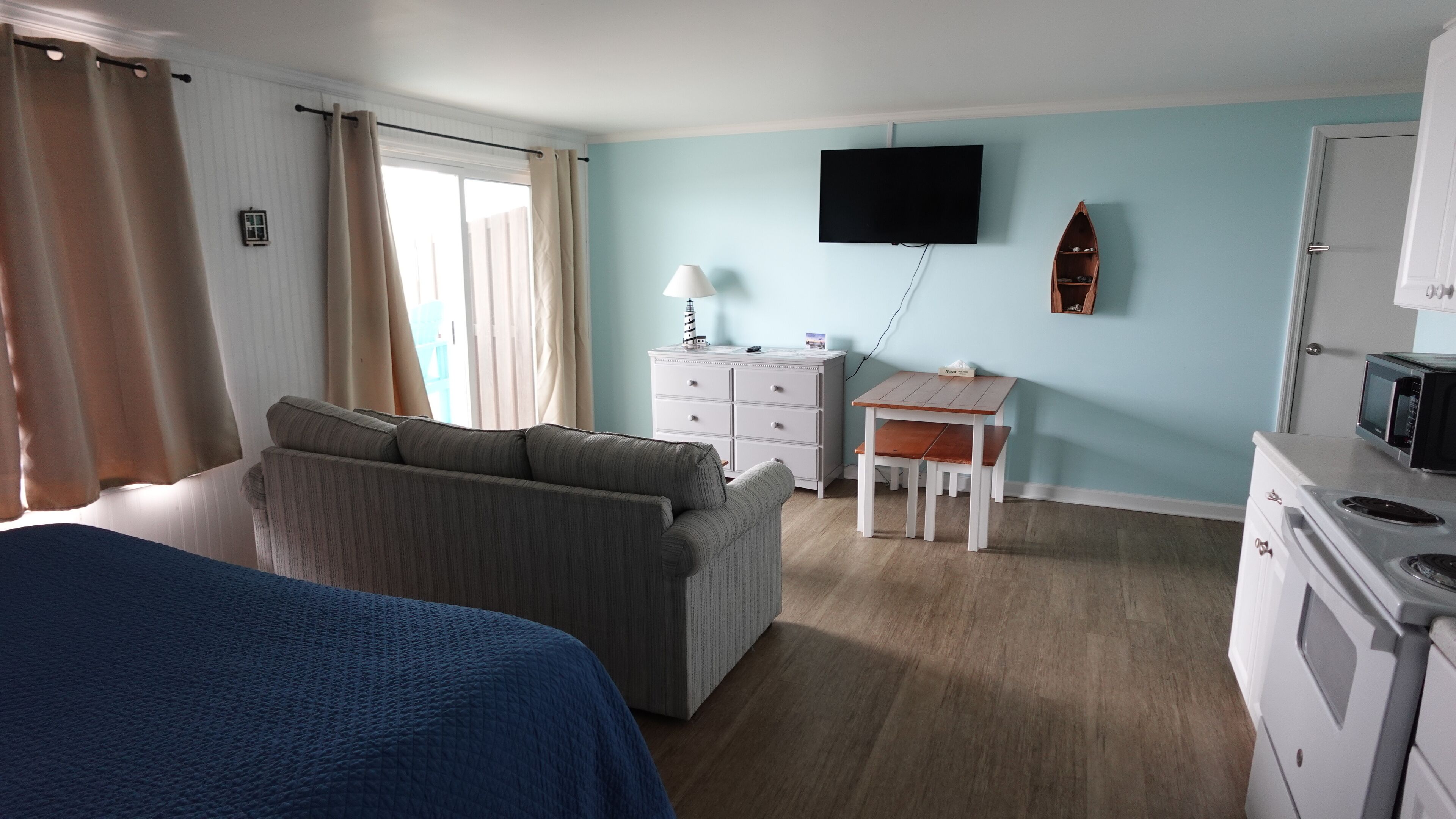 A room with a bed, a sofa, a desk, a television, and a microwave.