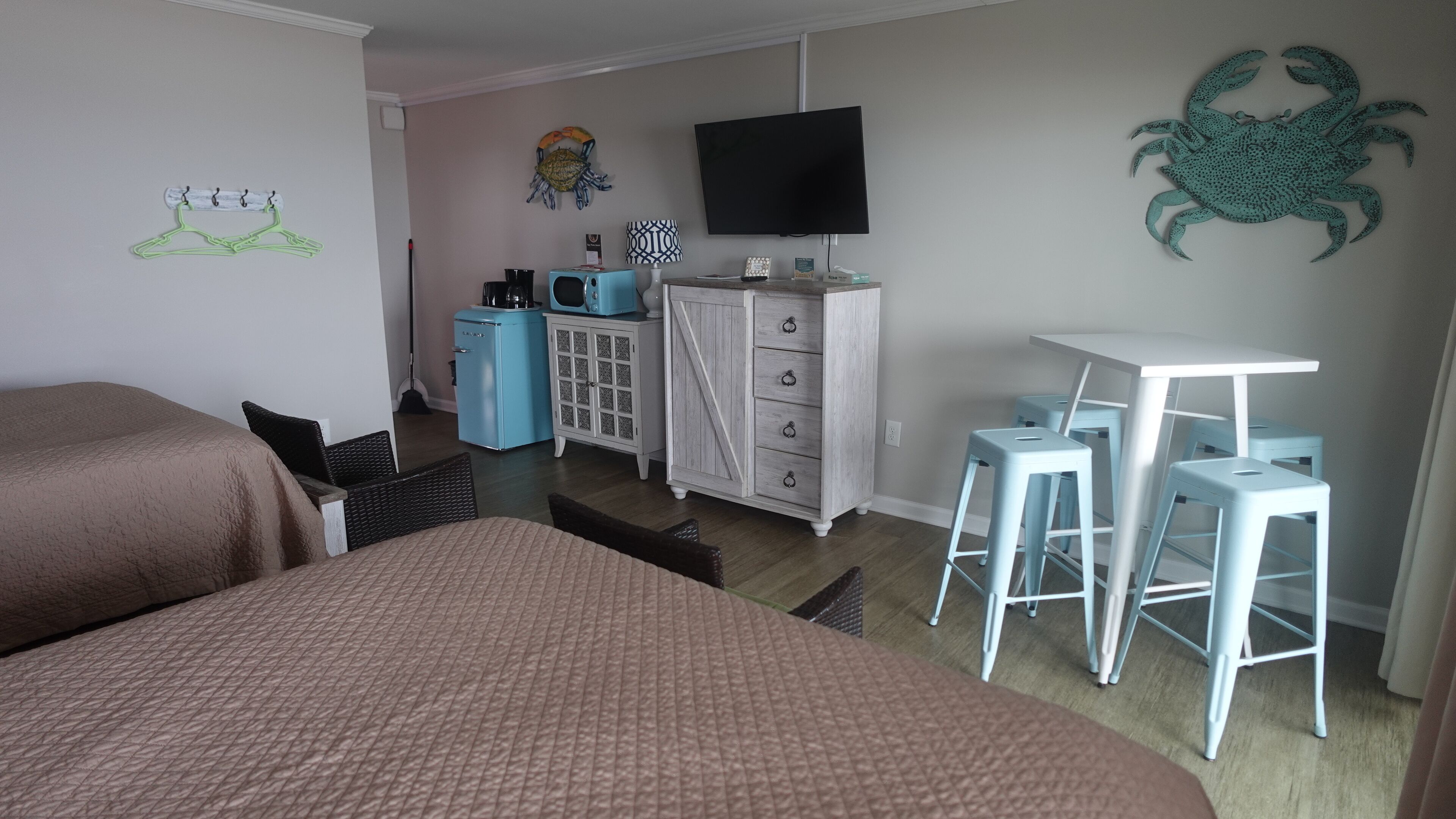 Een slaapkamer met twee bedden, een televisie, een kledingkast, een bureau met krukjes en een kunstwerk aan de muur.