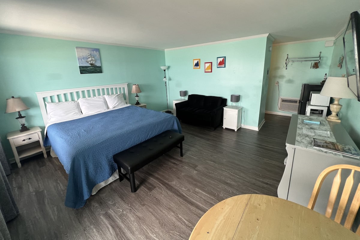 A room with a bed, bedside tables, a bench, a desk, a chair, and a small table.