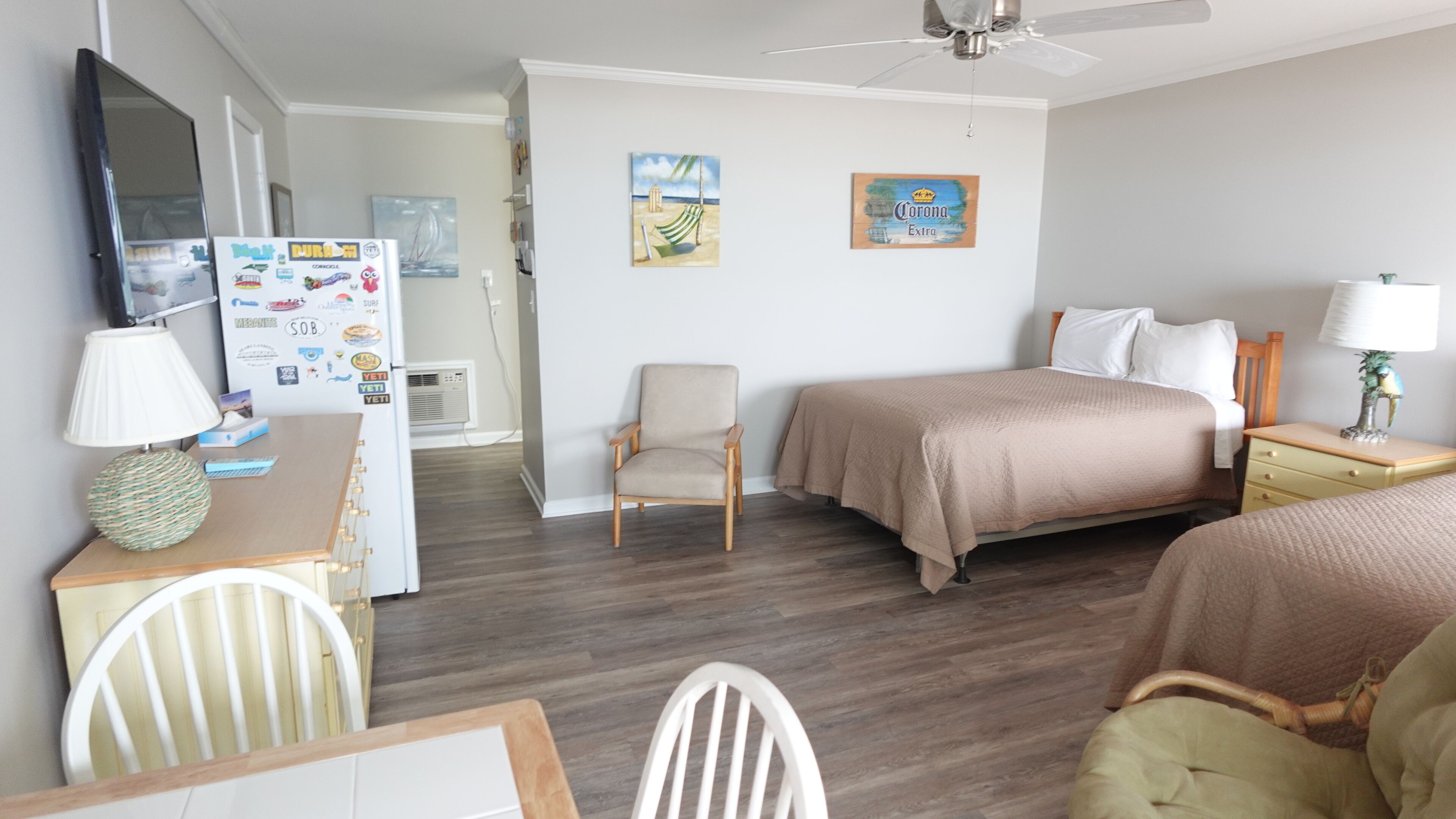 A compact hotel room with a bed, a desk, a chair, a refrigerator, and a ceiling fan.