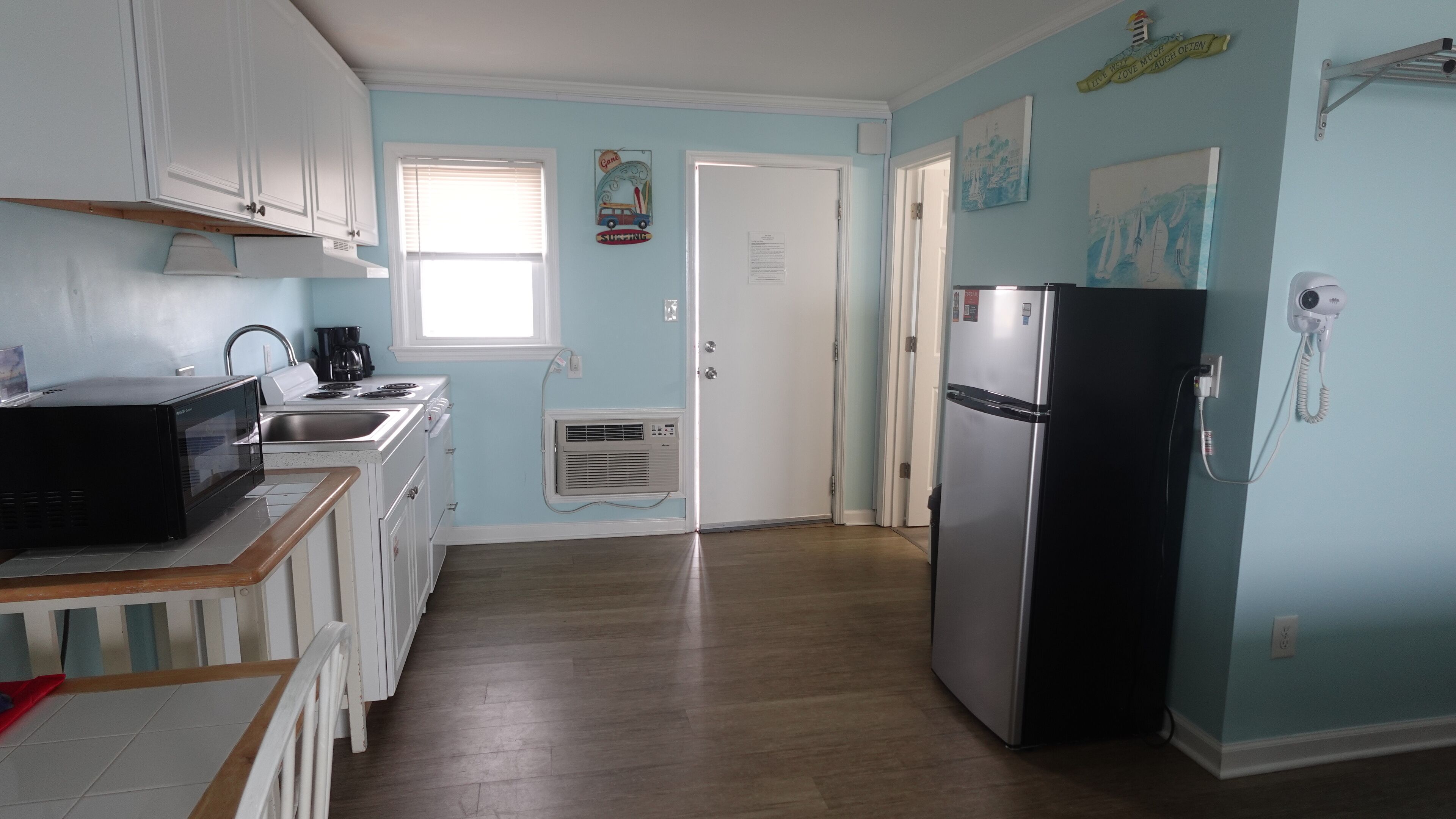 Una cocina con armarios blancos, un refrigerador negro y una ventana con persianas.