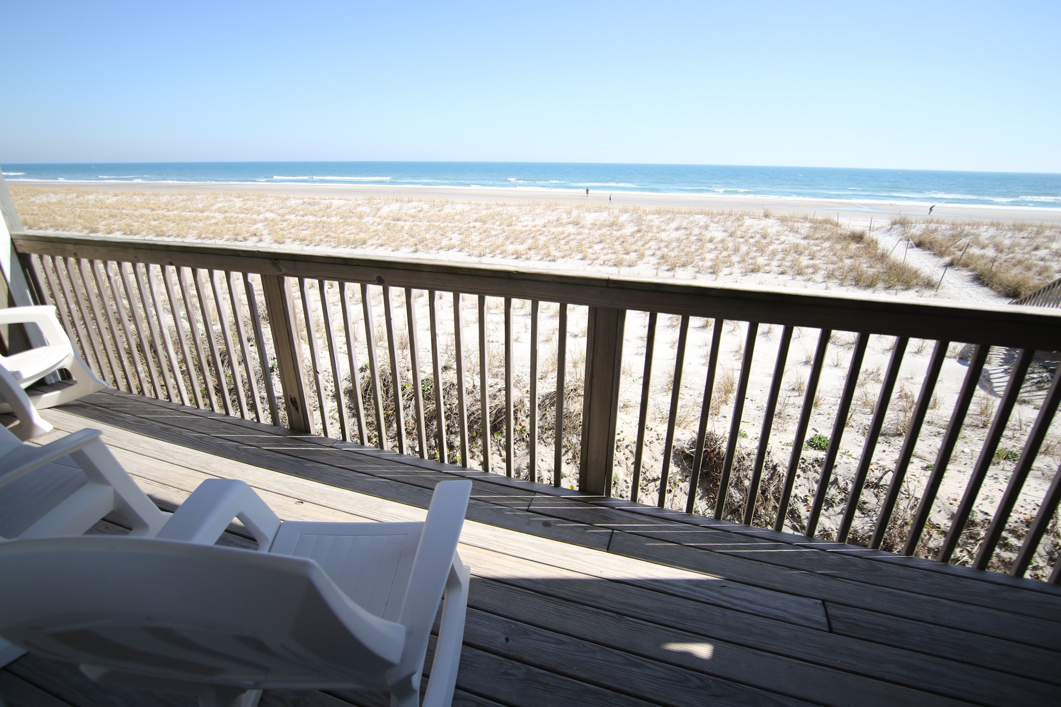 A wooden deck with white lounge chairs overlooking a beach with sand dunes and the ocean.