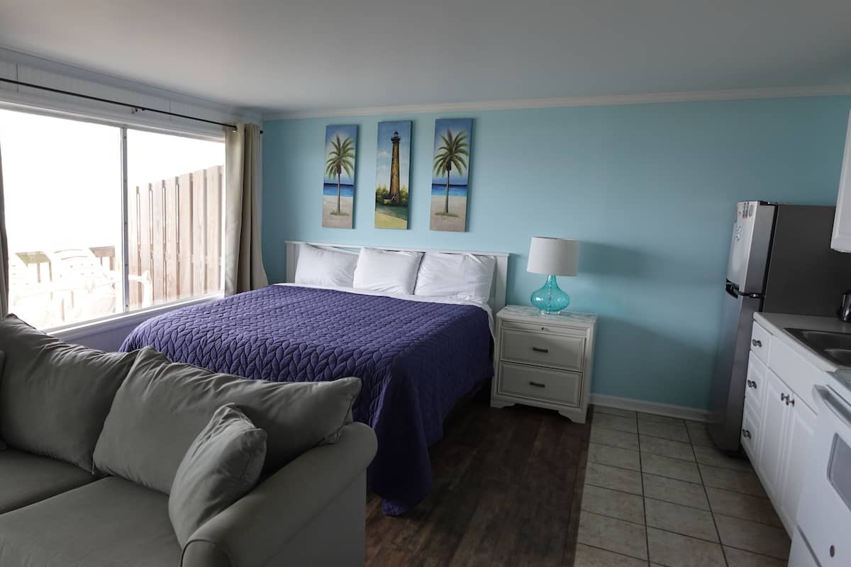 A bedroom with a bed, a nightstand, a lamp, a couch, and a view of the outside.