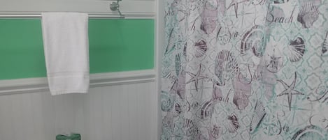 Une salle de bain avec des toilettes, un mur vert, un tableau au-dessus des toilettes et un rideau de douche orné de motifs marins.