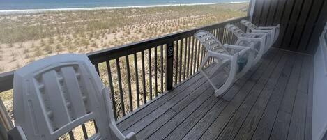 A wooden deck with white plastic chairs overlooking a beach.