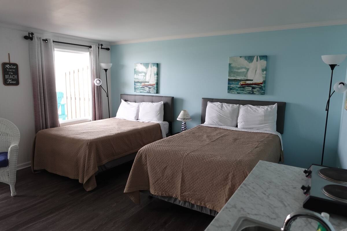 A hotel room with two beds, a dining area, and a view of the sea.