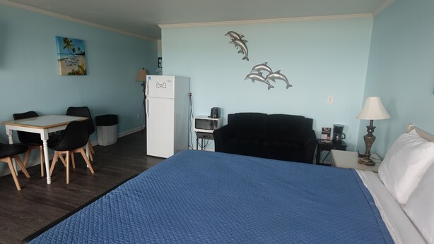 A hotel room with a bed, a desk with chairs, a refrigerator, a microwave, a coffee maker, and a lamp.