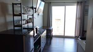 A compact living space with a kitchenette, a dining area, and a sliding glass door leading to a balcony. - Sea Vista Motel (Holly Ridge)
