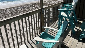 A wooden deck with turquoise chairs overlooking a beach.