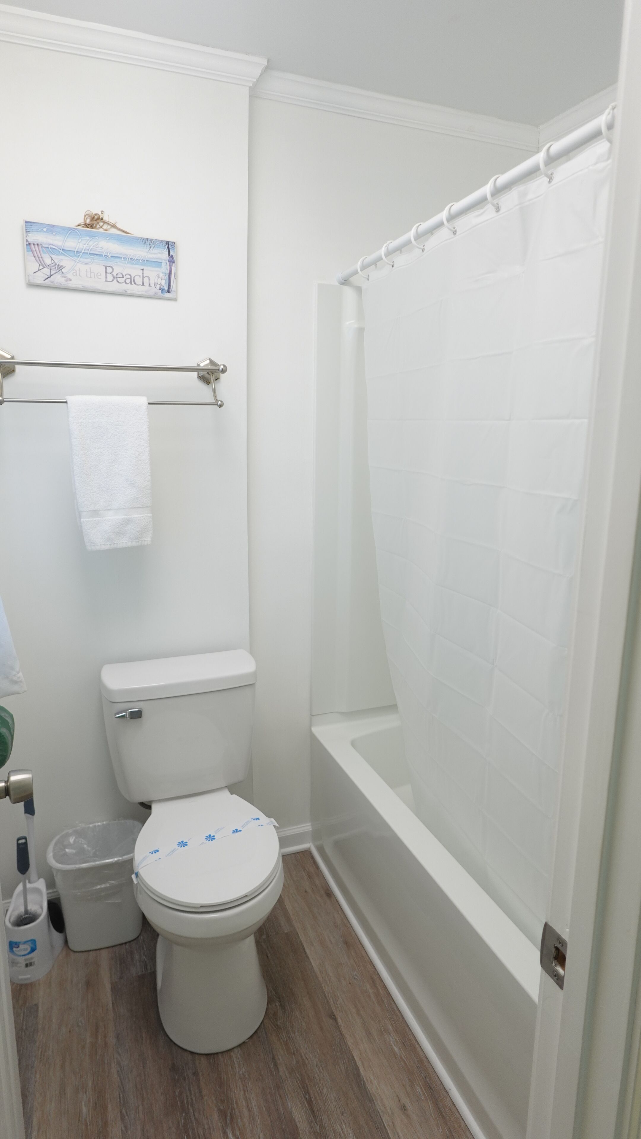 Un baño con inodoro, cortina de ducha, toallero y un cartel en la pared.