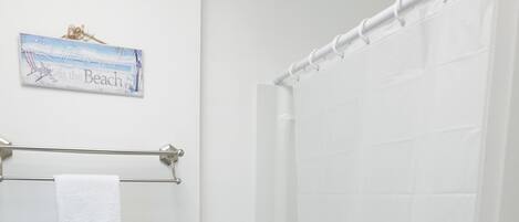 Un baño con inodoro, cortina de ducha, toallero y un cartel en la pared.