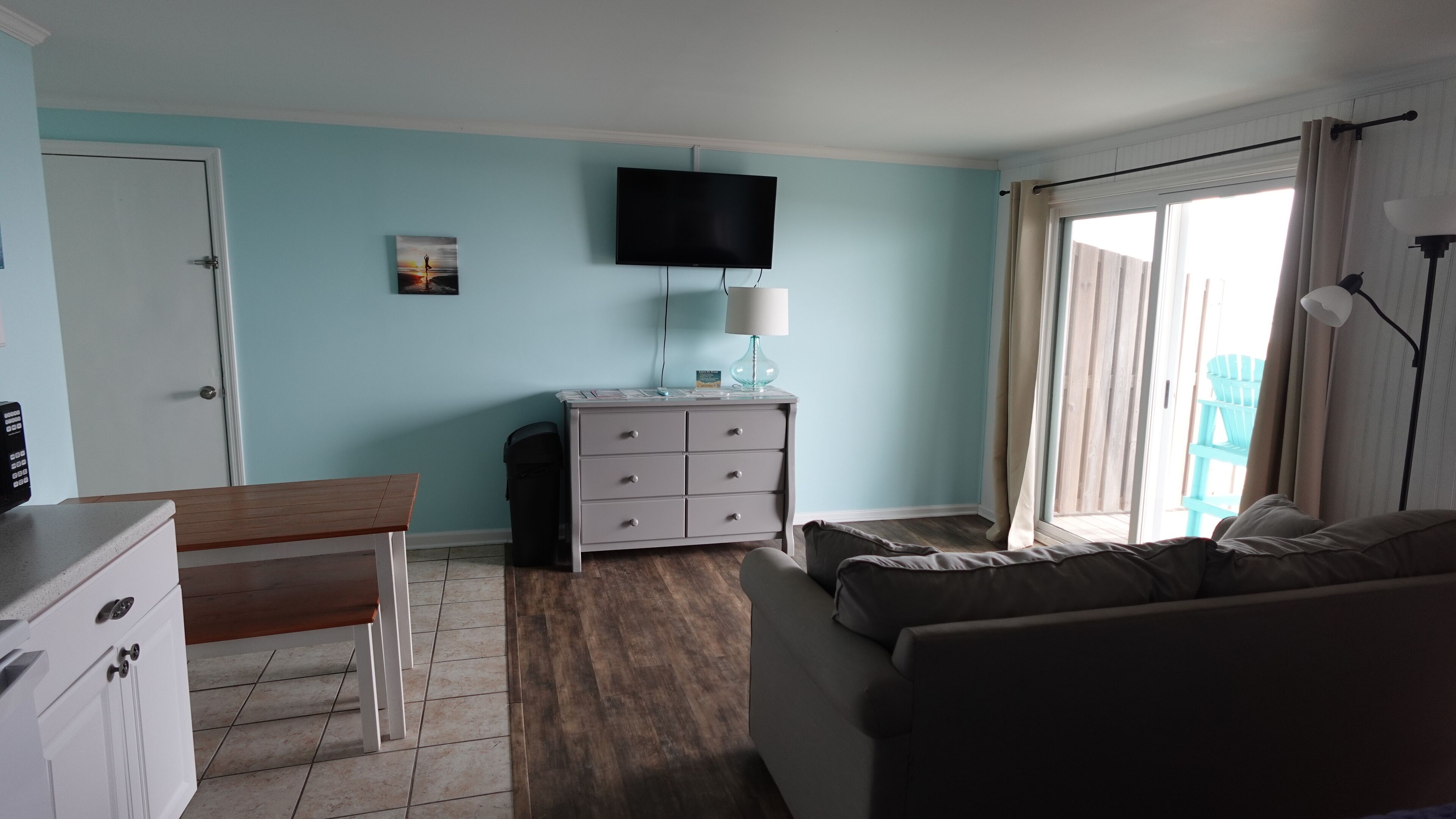 A bedroom with a bed, a desk, a chair, a dresser, a television, and a window with curtains.