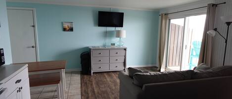 A bedroom with a bed, a desk, a chair, a dresser, a television, and a window with curtains.