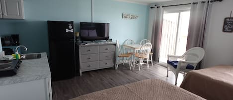 A compact hotel room with a kitchenette, a television, a dining area with a table and chairs, and a bed.
