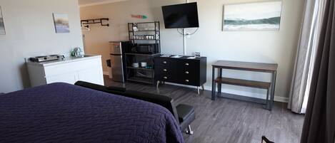 Habitación de hotel con cama, escritorio, televisión, kitchenette y ventana con cortinas.