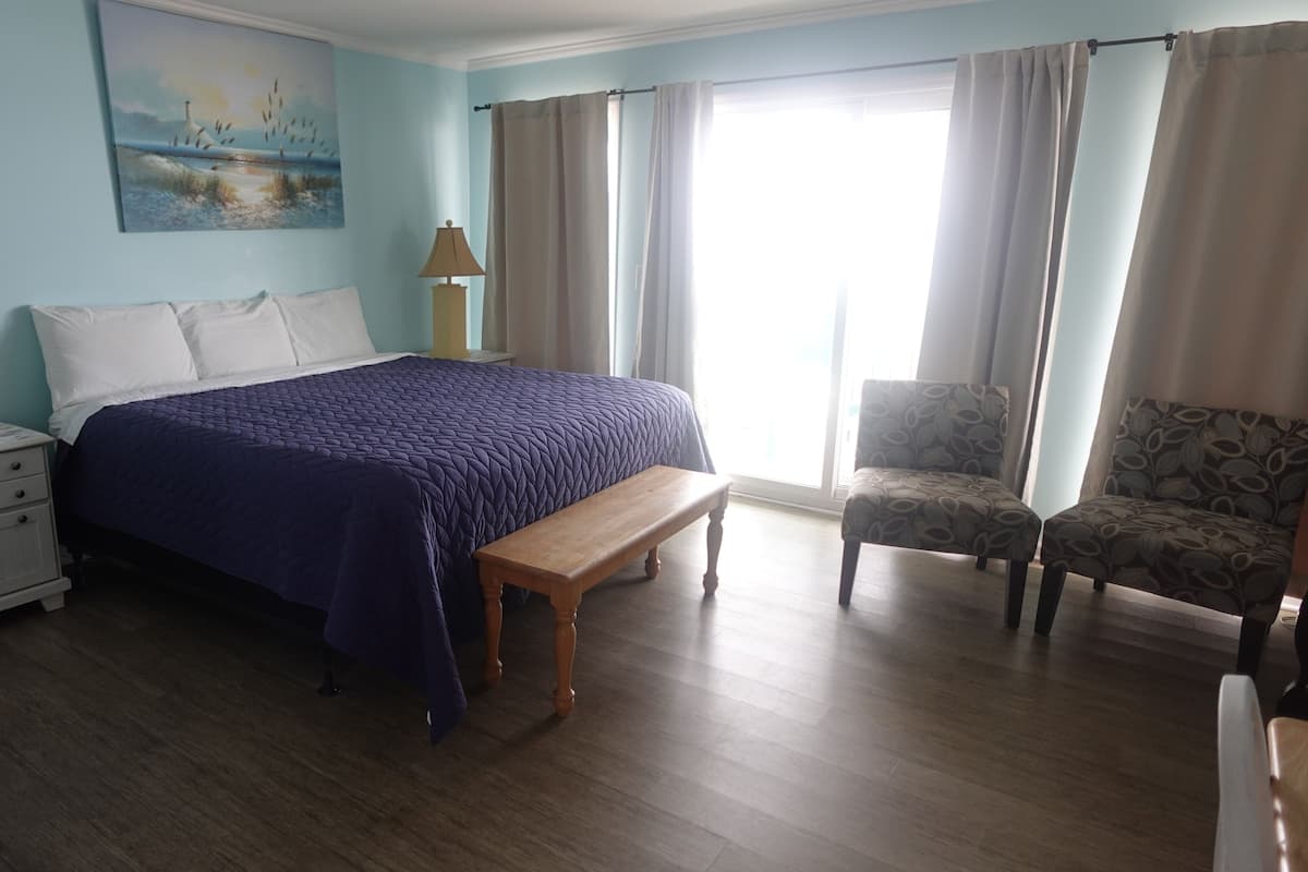 A bedroom with a bed, bedside tables, a bench, a chair, and a painting on the wall.
