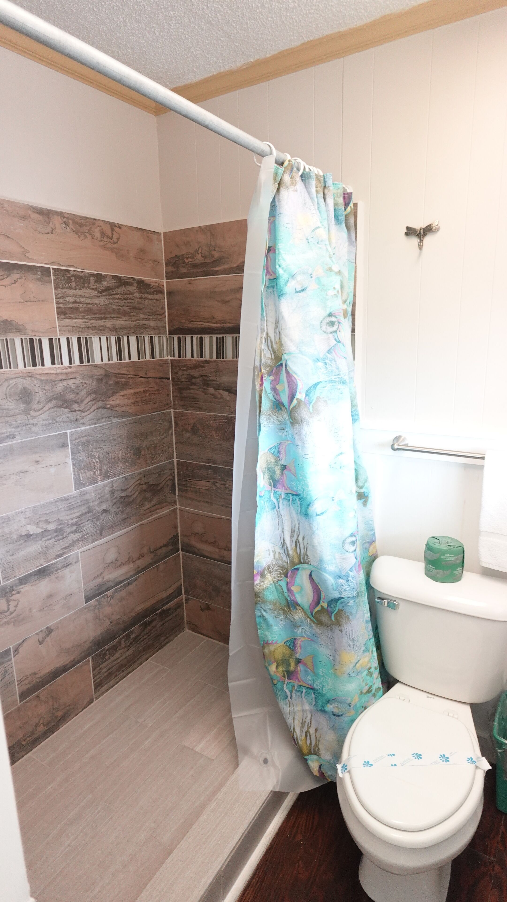 Ein Duschbereich mit gemustertem Duschvorhang, einer Toilette und einer Wand mit einer Kombination aus Holz- und Steinfliesen.