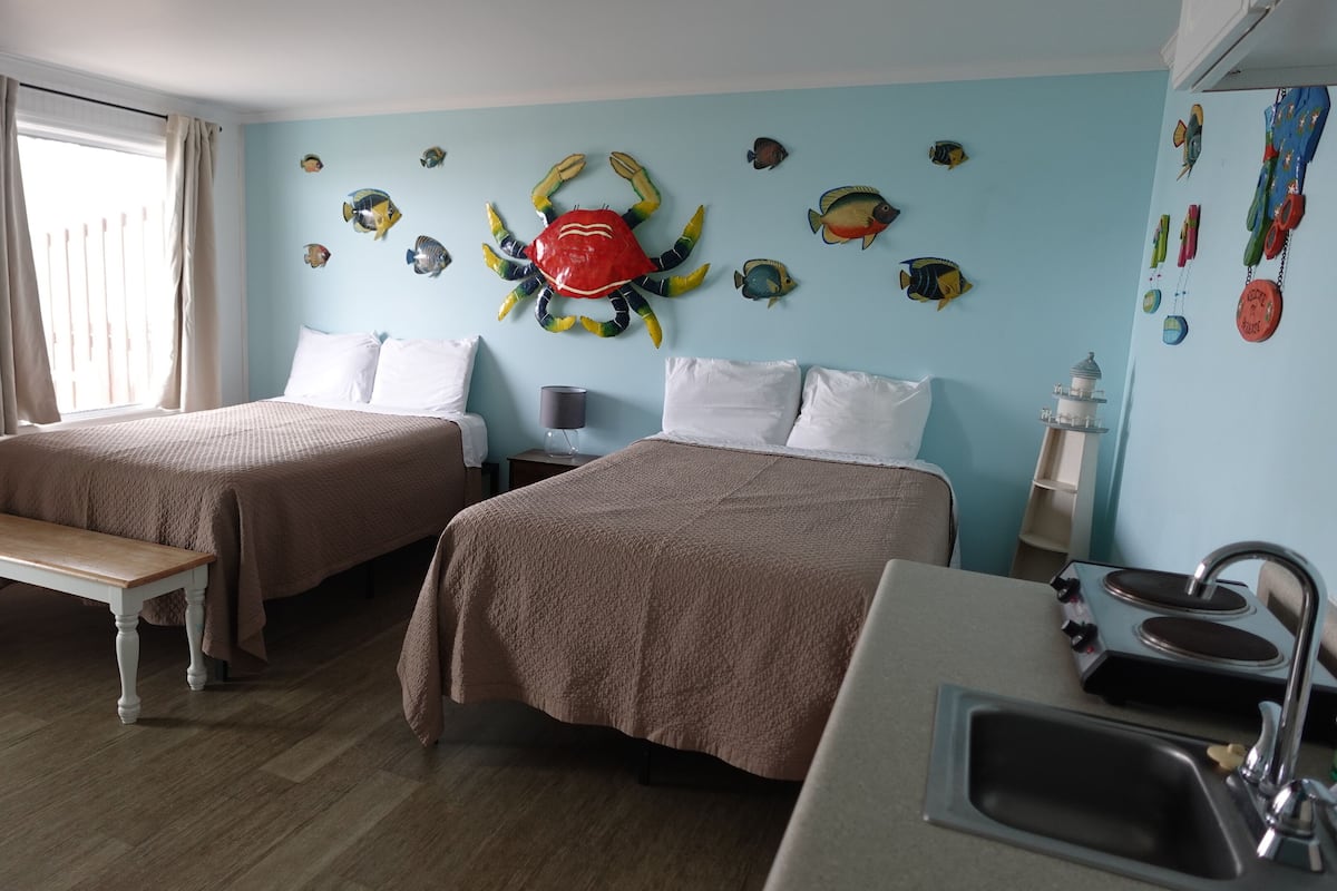 A hotel room with two beds, a bench, a sink, and decorative fish wall art.