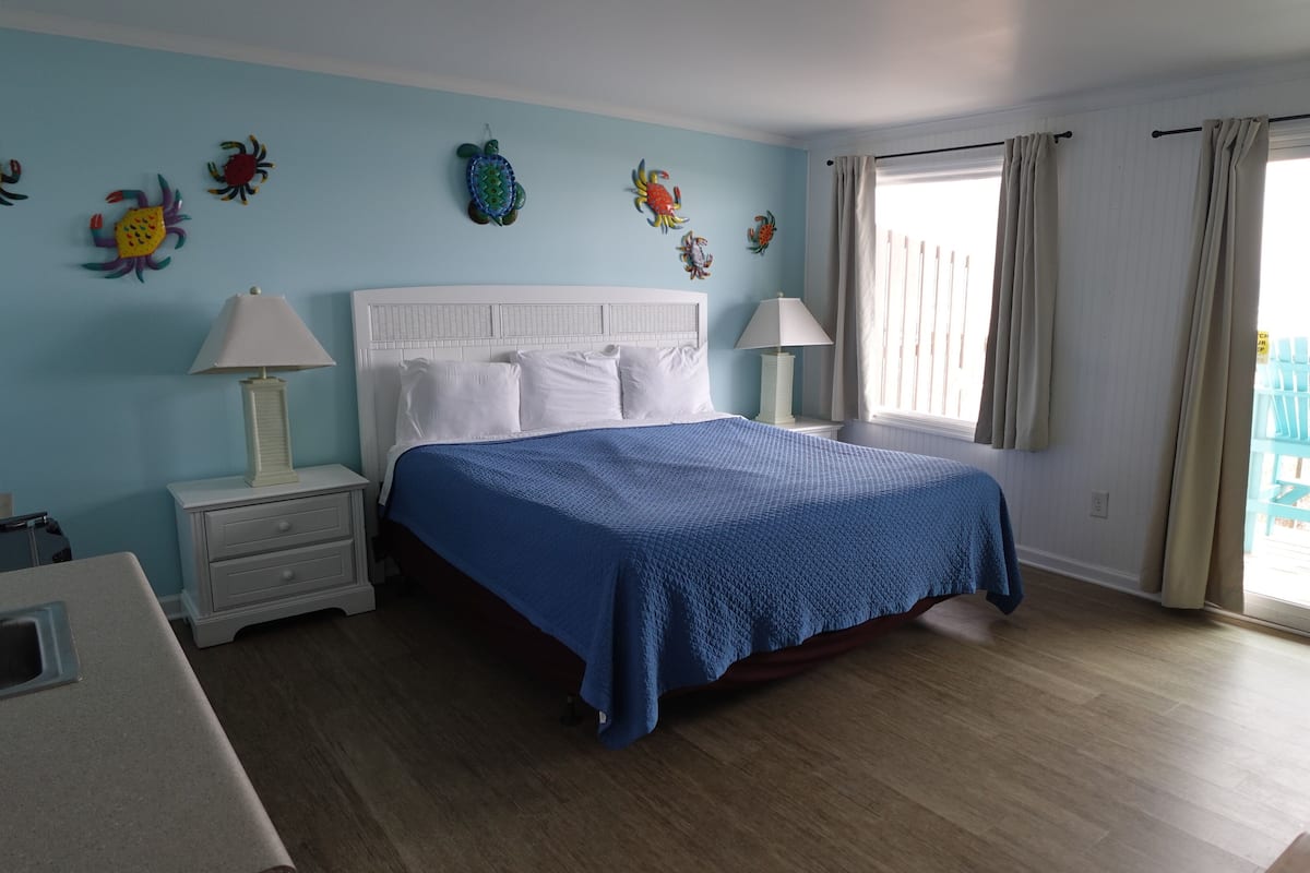 A bedroom with a bed, two bedside tables, a nightstand, a window with curtains, and a balcony with a chair.
