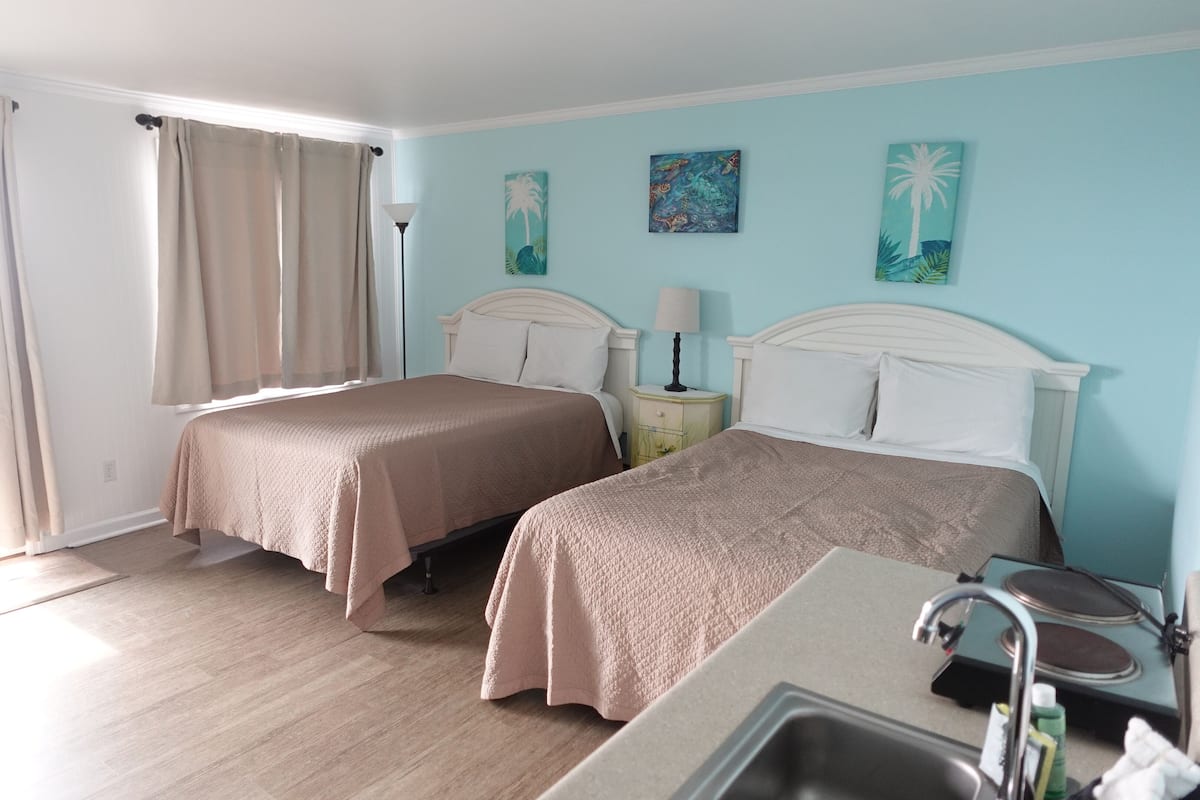 A hotel room with two beds, a sink, and a window with curtains.