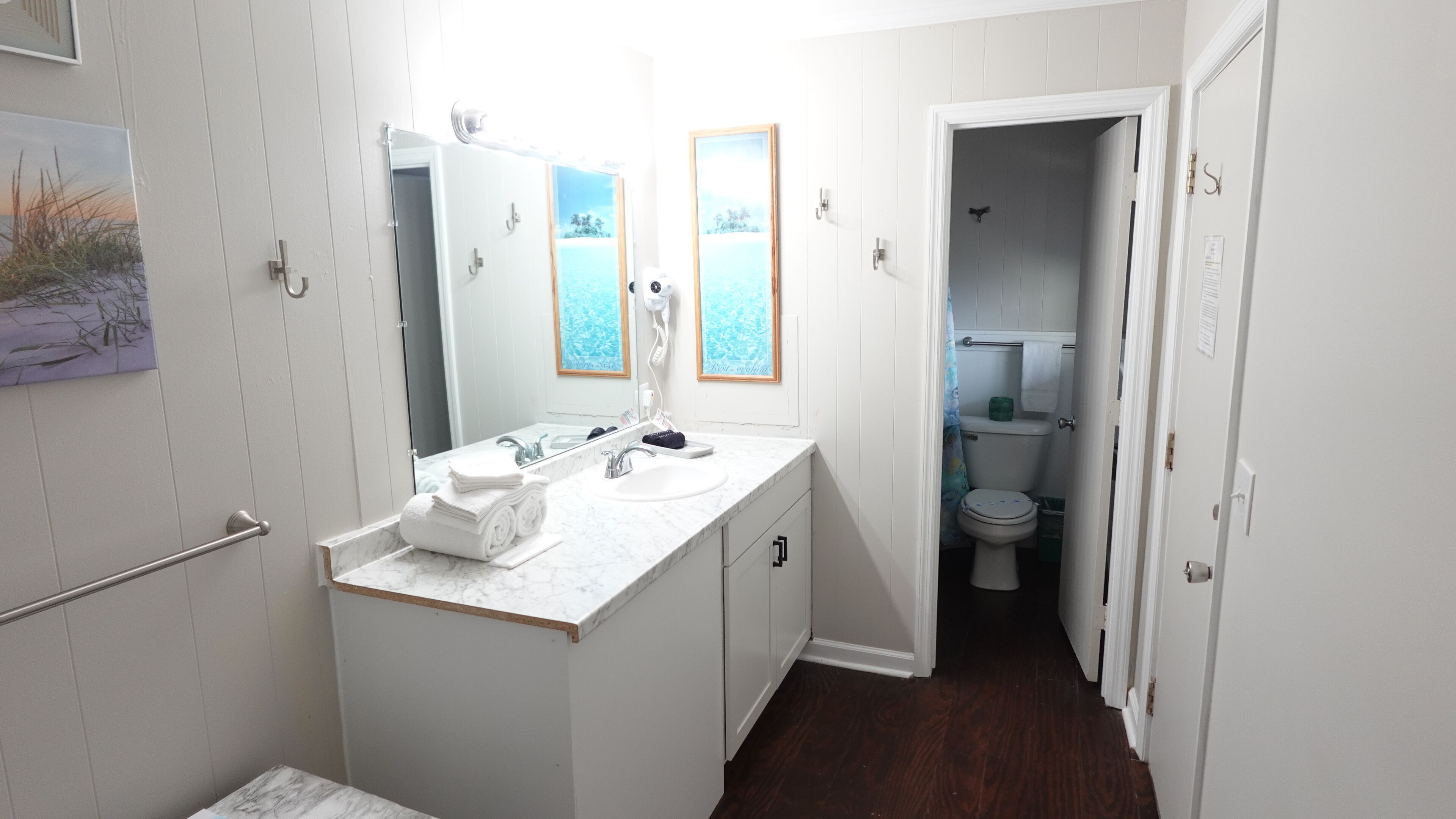 A bathroom with a white vanity, a large mirror, and a toilet visible through an open door.