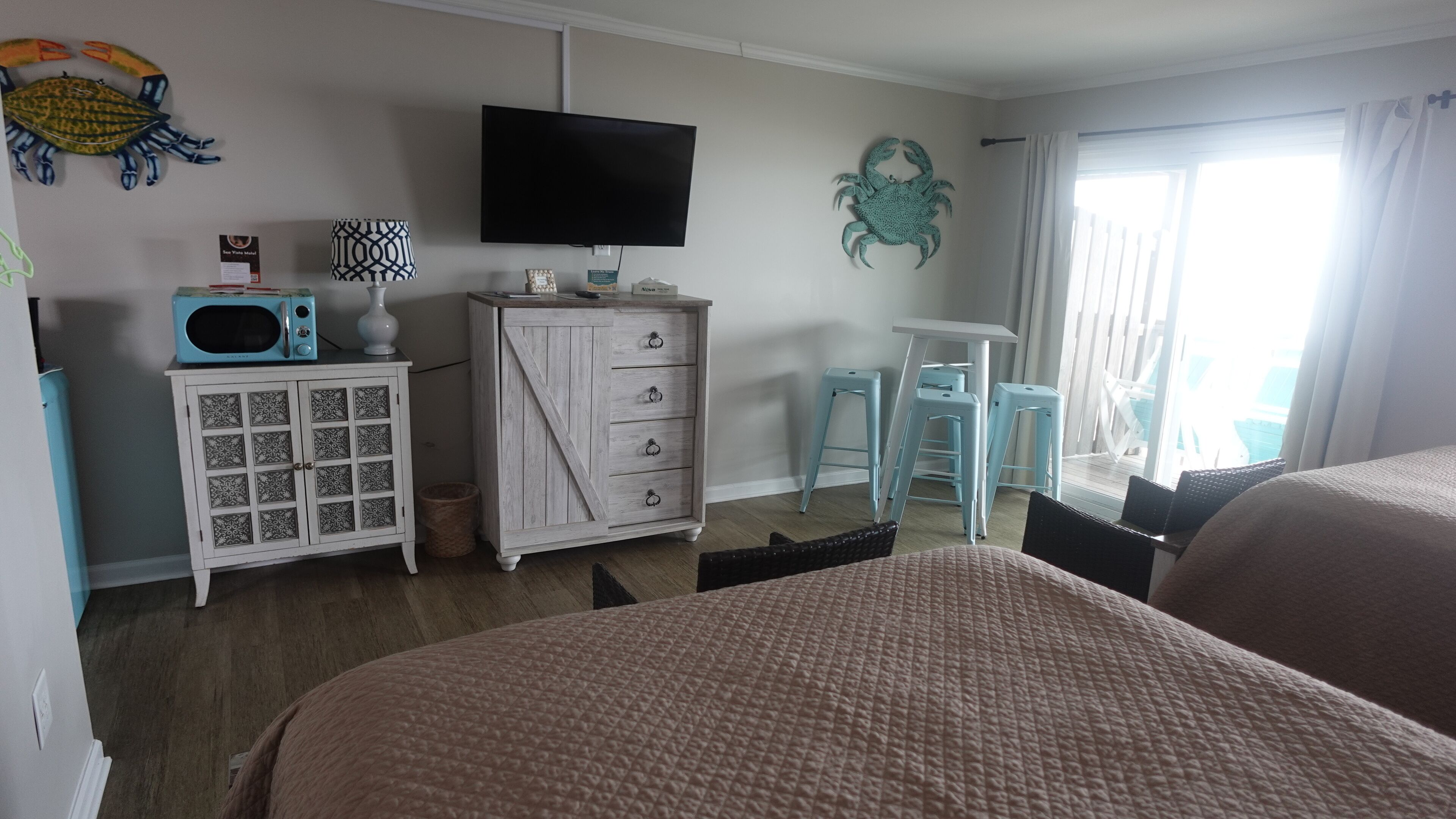 A hotel room with two beds, a TV, a wooden dresser, and a window with curtains.