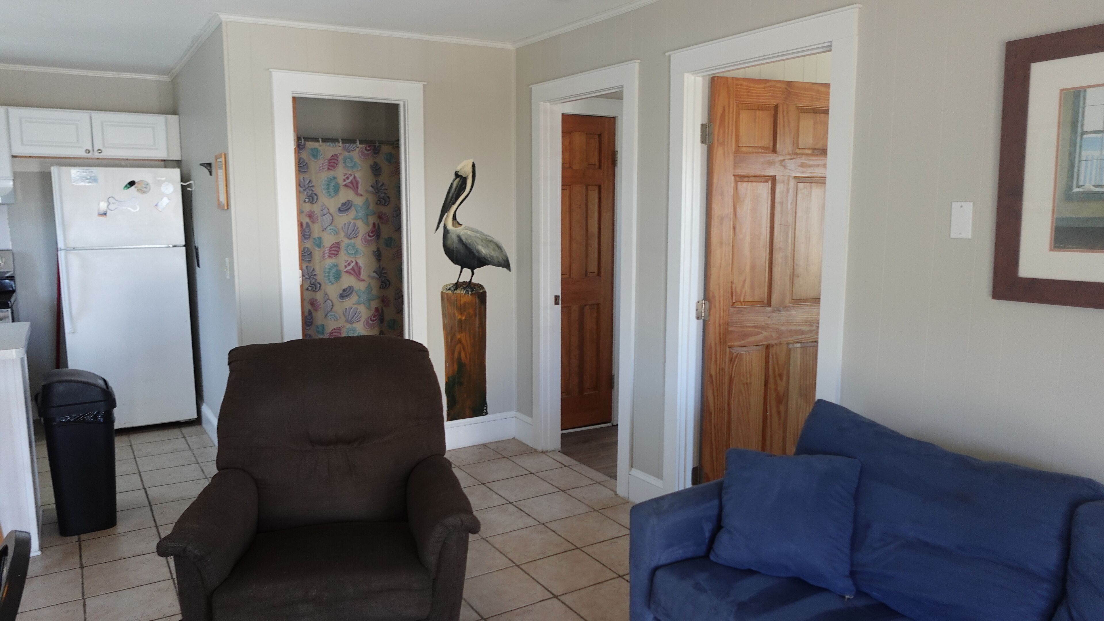 A living room with a brown armchair and a blue sofa. There is a wooden door and a wall with a framed picture.