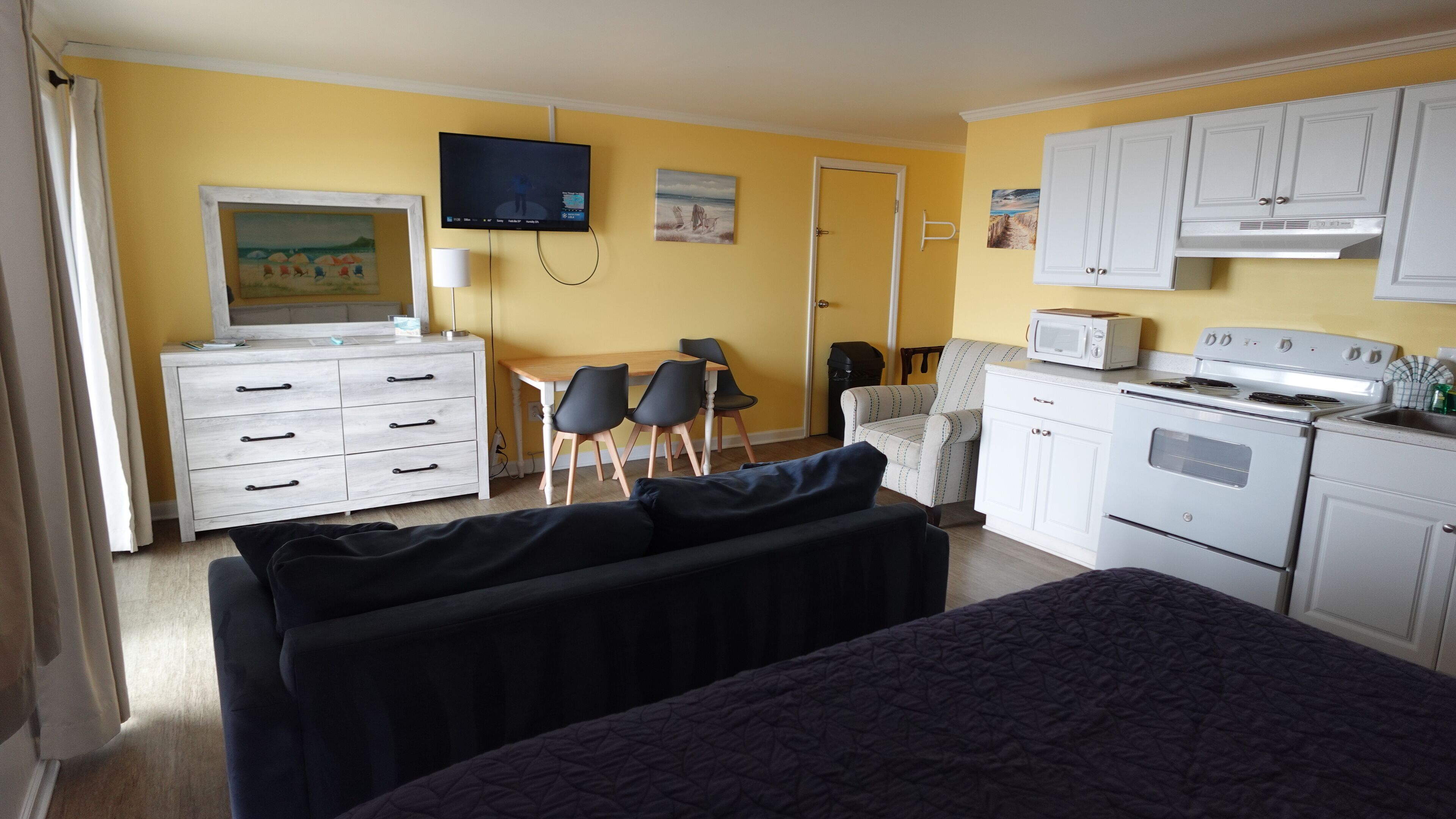 A compact room with a bed, a desk, a chair, a television, a microwave, and a stove.
