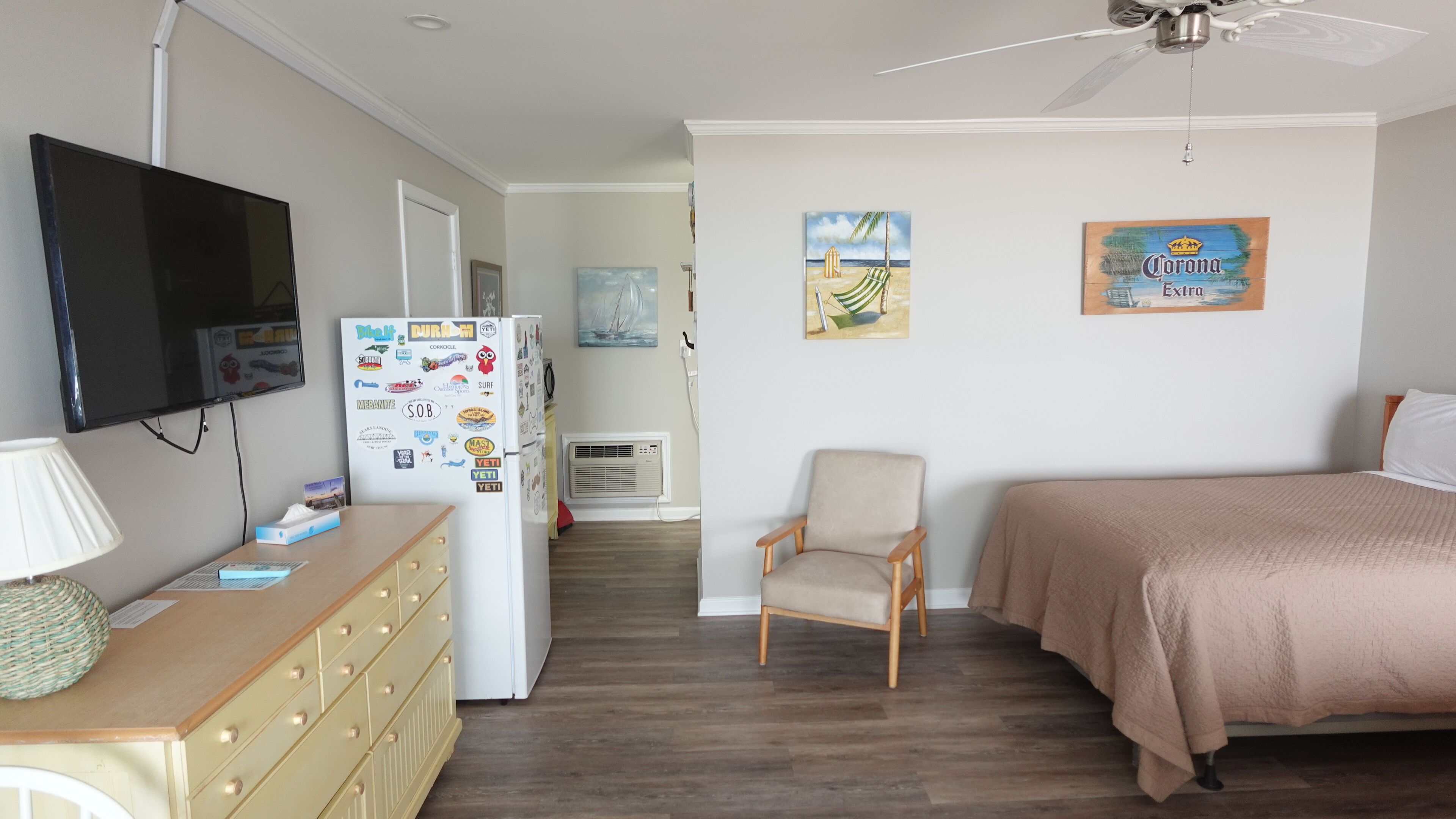 A bedroom with a bed, a chair, a TV, and a refrigerator with various magnets.