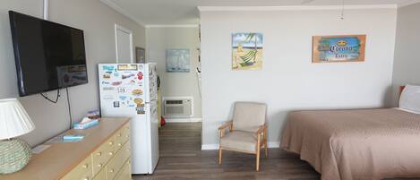 A bedroom with a bed, a chair, a TV, and a refrigerator with various magnets.
