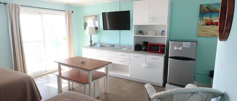 A compact kitchen with a dining table, white cabinets, a microwave, and a refrigerator.