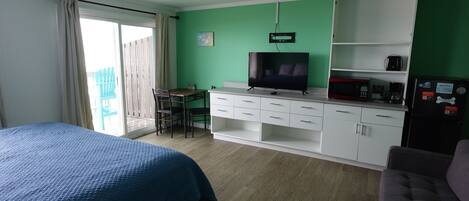 A room with a bed, a desk with a chair, a television, a microwave, and a refrigerator.