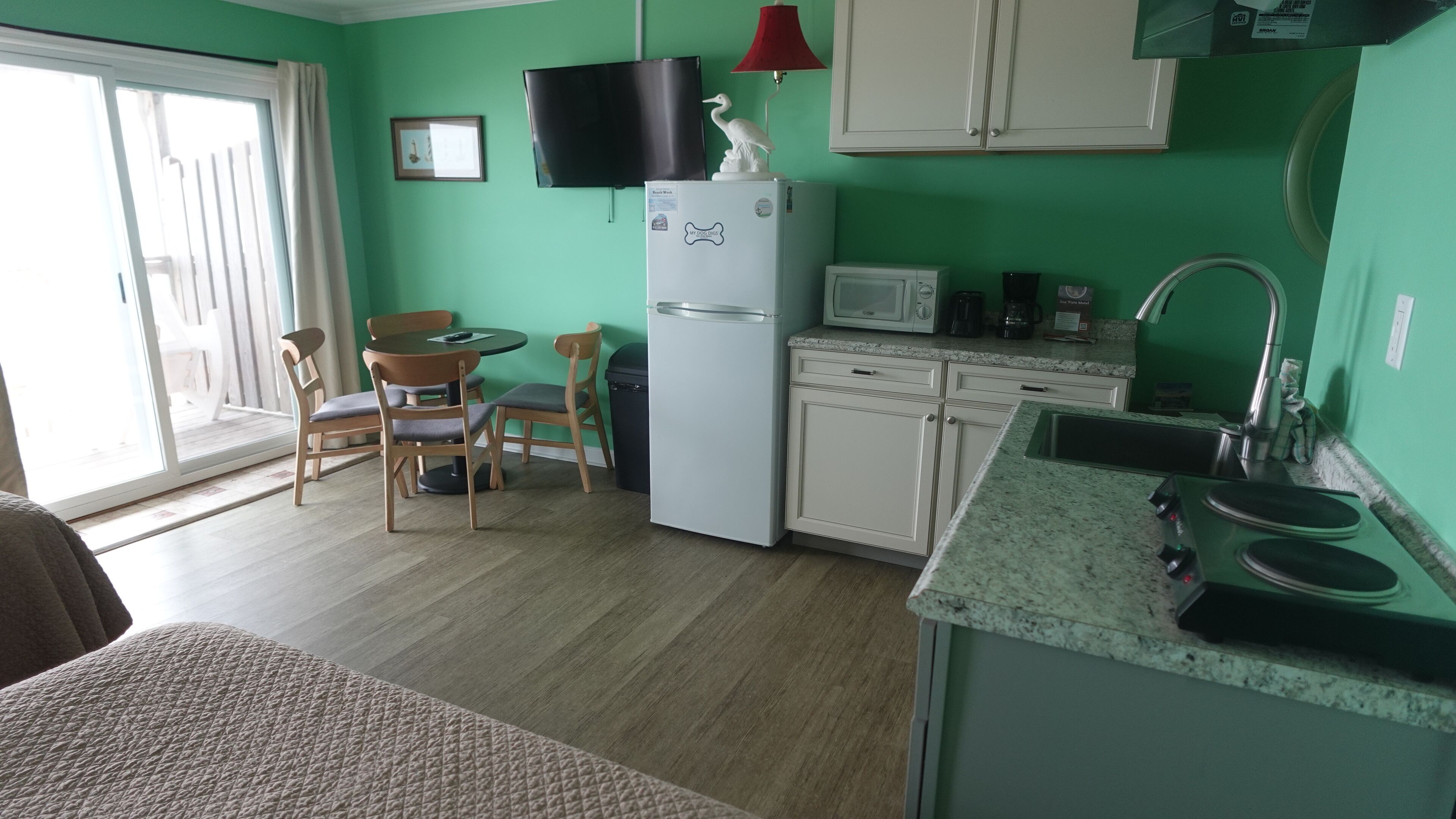A compact kitchen with a refrigerator, microwave, and sink. There is a dining area with chairs and a table.