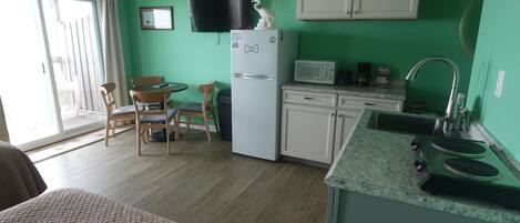 A compact kitchen with a refrigerator, microwave, and sink. There is a dining area with chairs and a table.