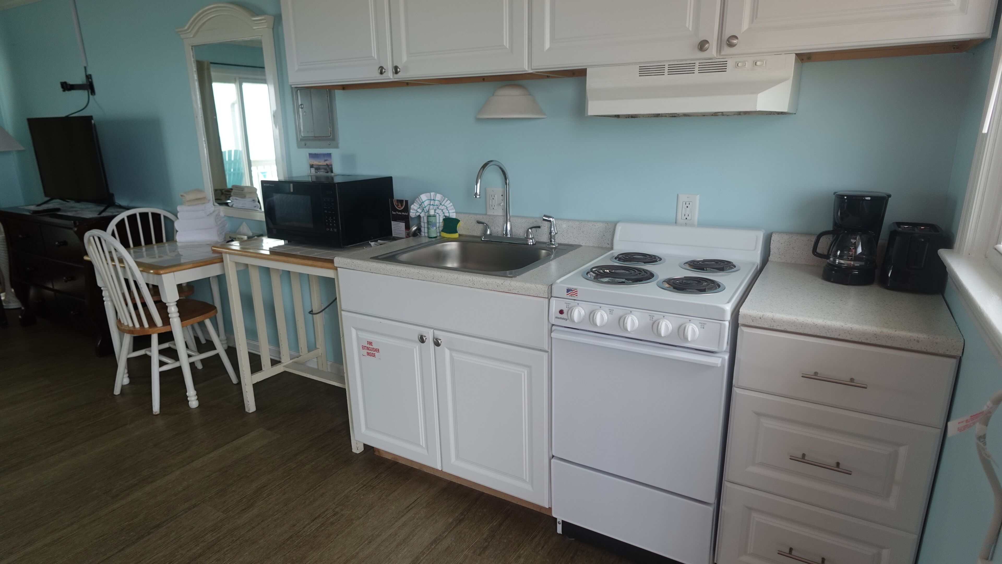 A compact kitchen with white cabinets, a stove, a sink, and a microwave.