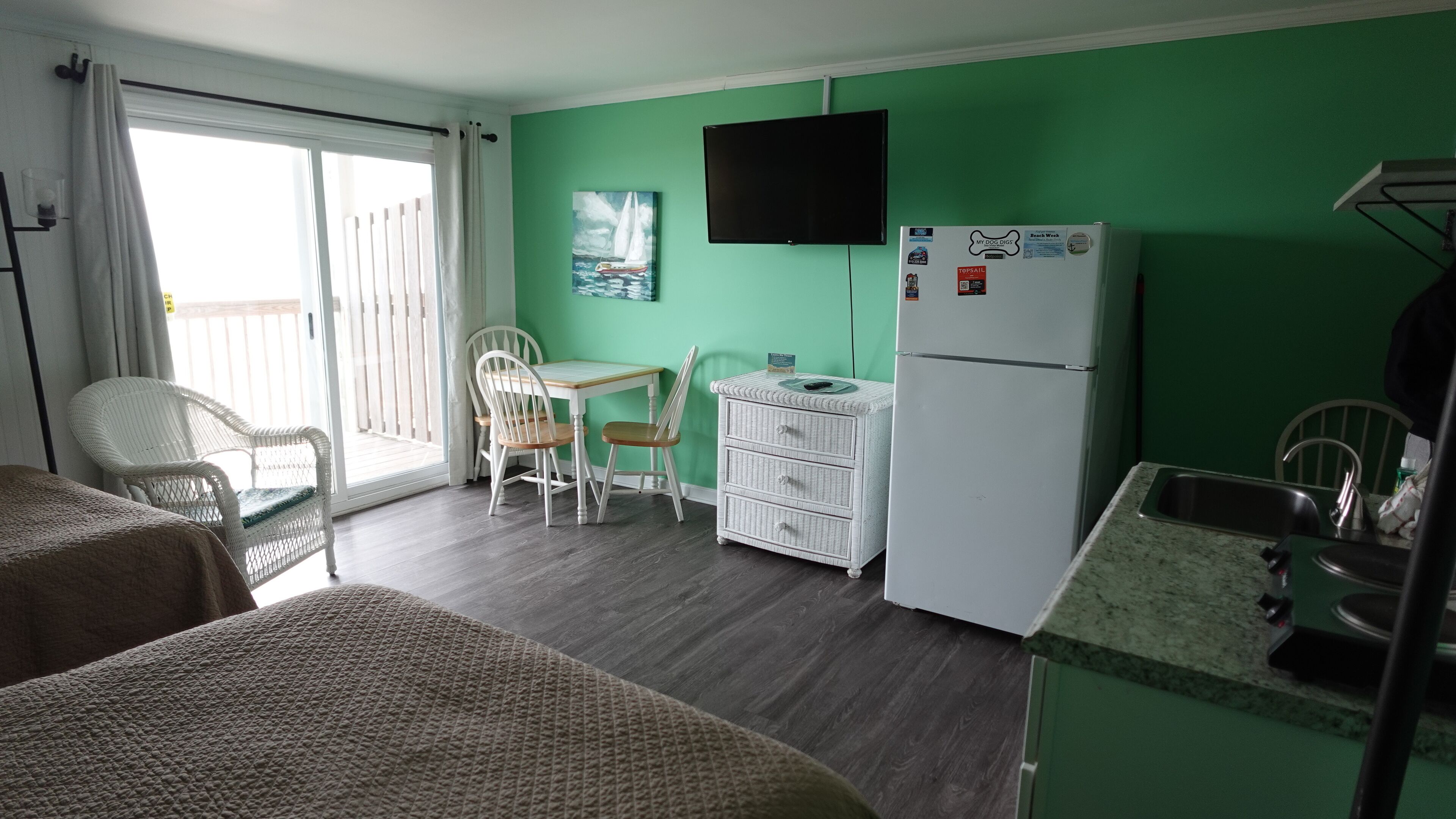 A room with a dining table, two chairs, a white refrigerator, and a television mounted on the wall.