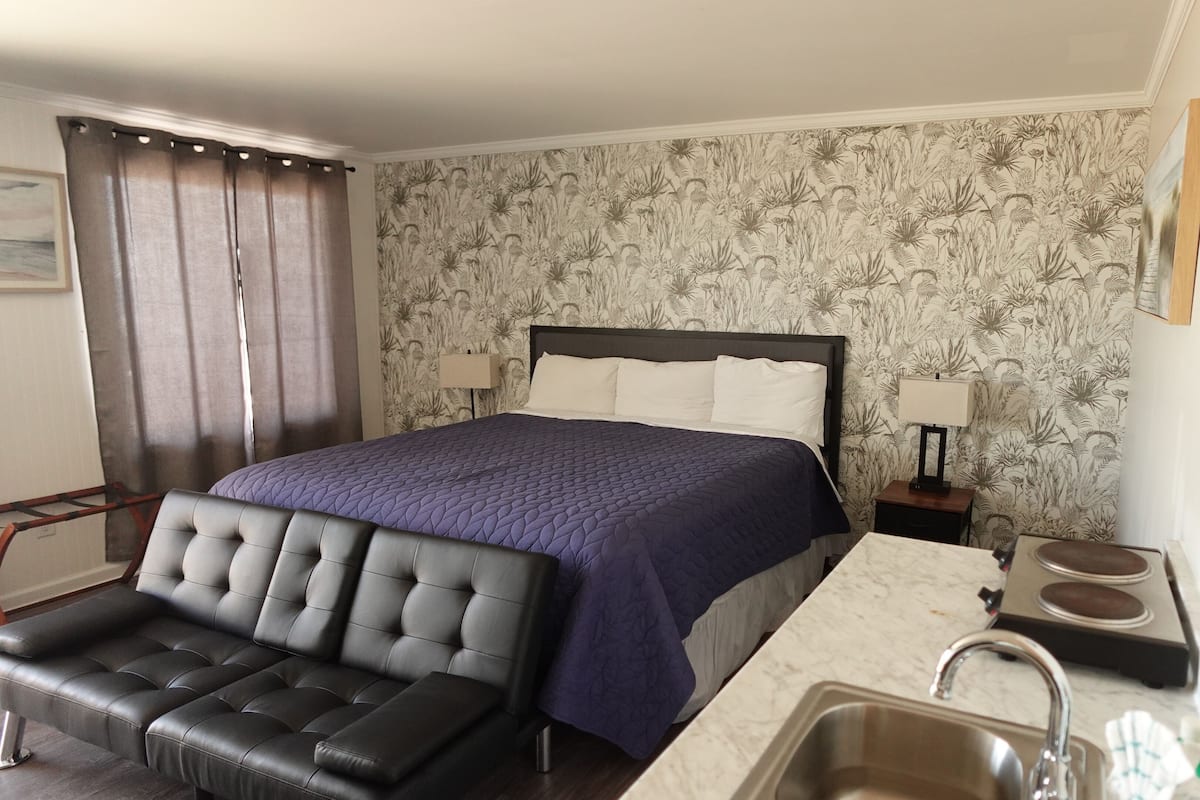 A hotel room with a bed, a chair, a sink, and a mirror.
