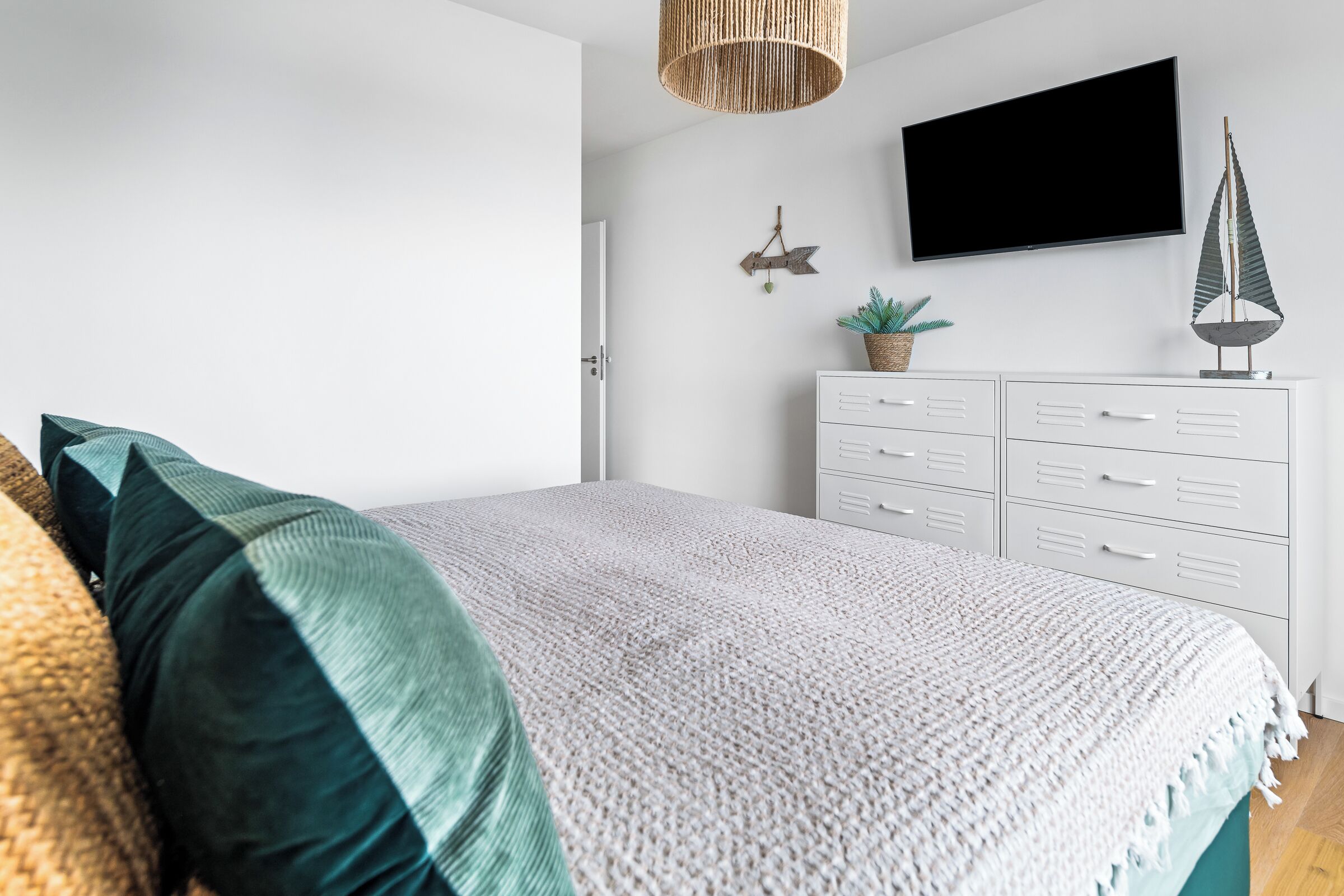 A bedroom with a bed, white dresser, television, and decorative items.