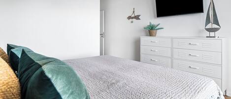 A bedroom with a bed, white dresser, television, and decorative items.