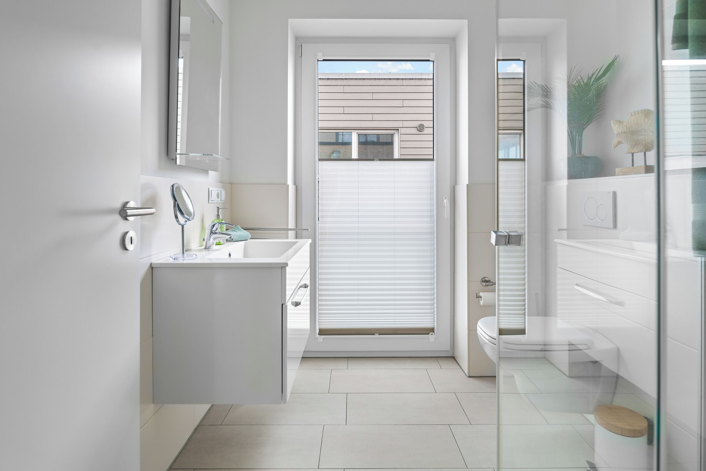 Un baño moderno con lavamanos, espejo e inodoro blancos.