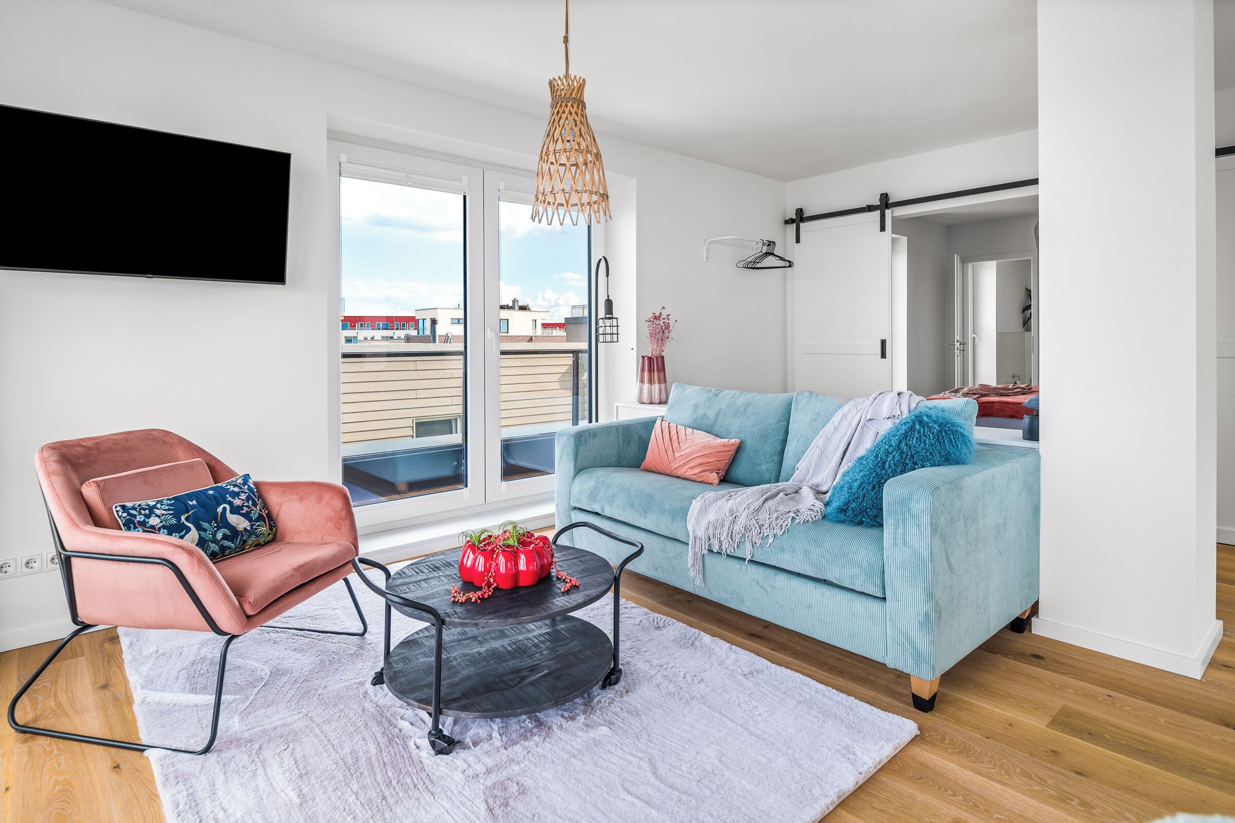 Un salon moderne avec un canapé, un fauteuil et une table basse, une grande fenêtre offrant une belle vue et un luminaire suspendu.